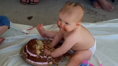 Маленькая девочка смешно ест свой первый торт